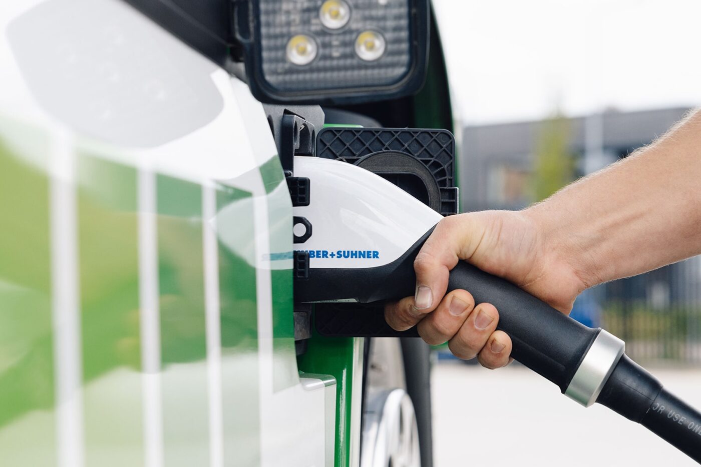 A human hand connects a charging cable into the charging port of an electric vehicle