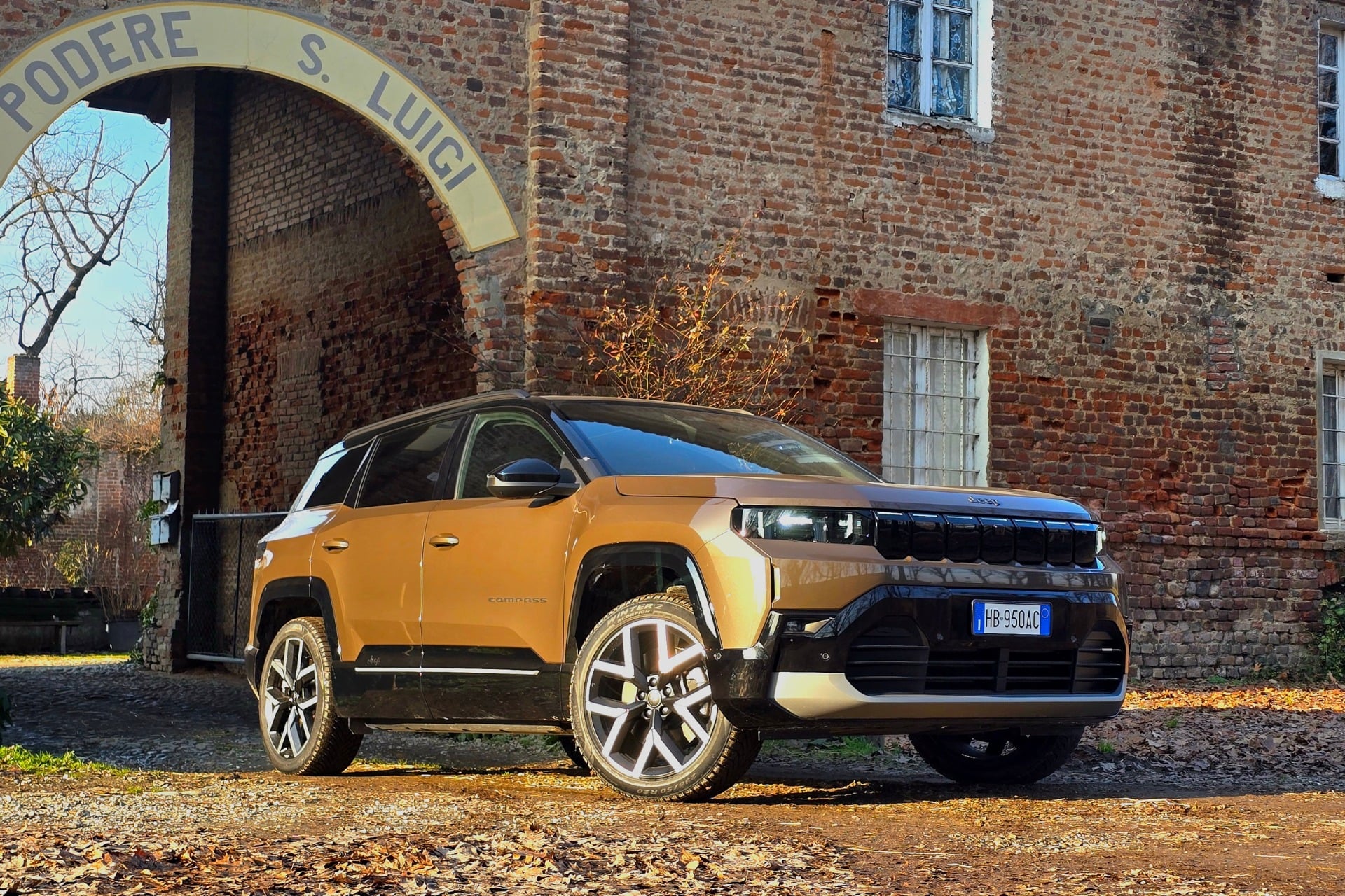 Essai Jeep Compass électrique marron cuivré garé devant une bâtisse ancienne en briques, illustrant les capacités de franchissement et le design baroudeur du SUV Stellantis.