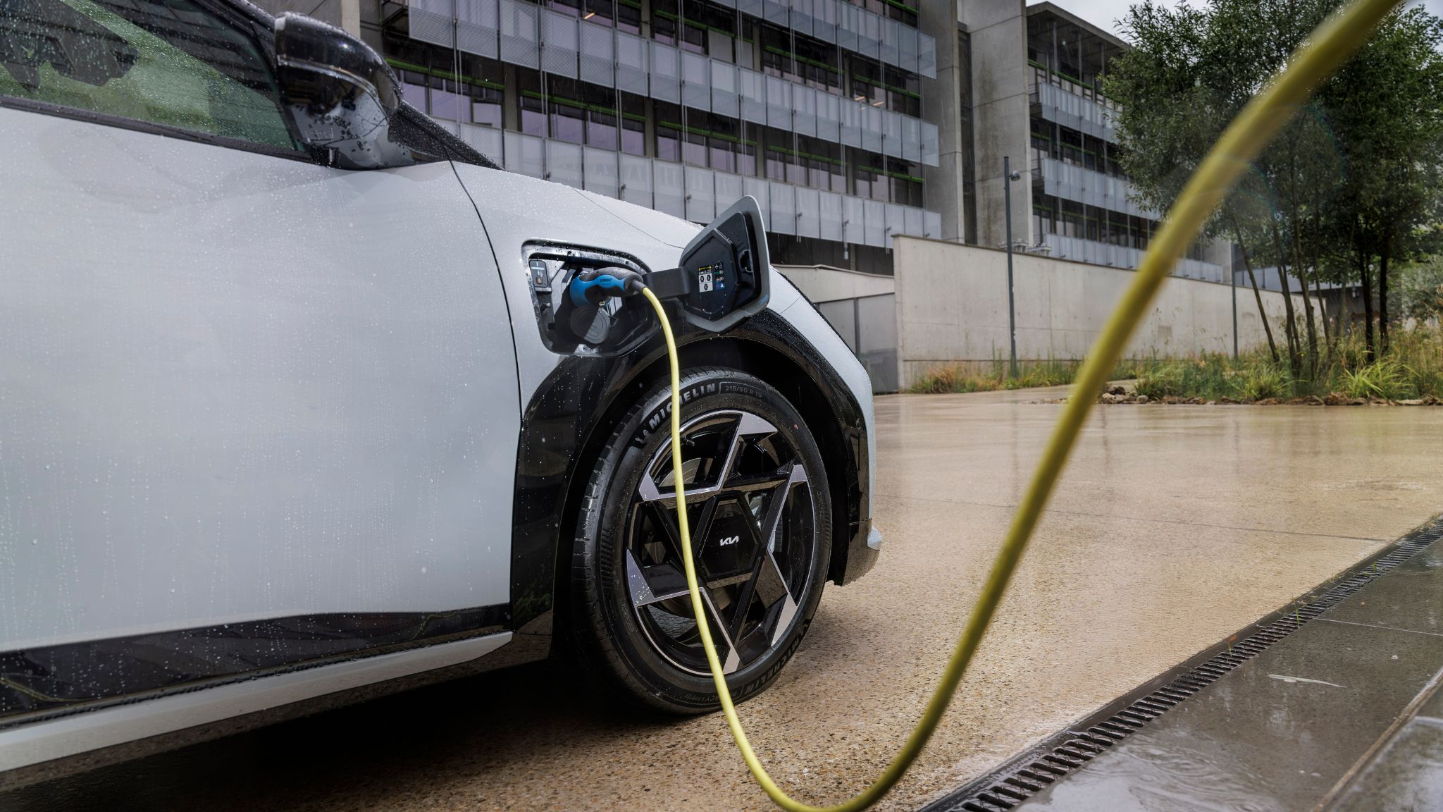 Kia EV4 en recharge avec câble branché sur la prise avant gauche, jante alliage visible.