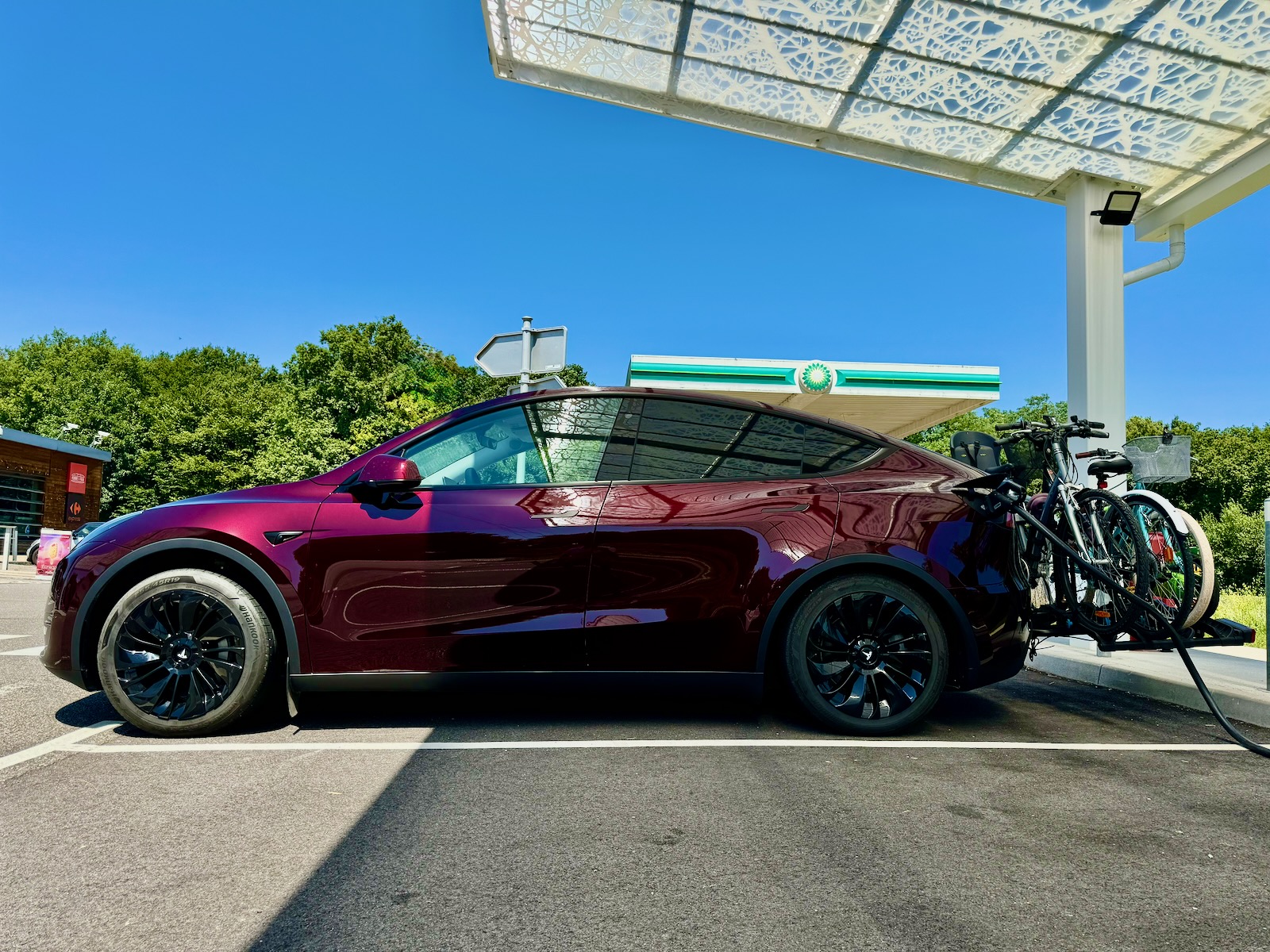 Tesla Model Y rouge équipée de vélos en cours de recharge à une borne sur la route des vacances.