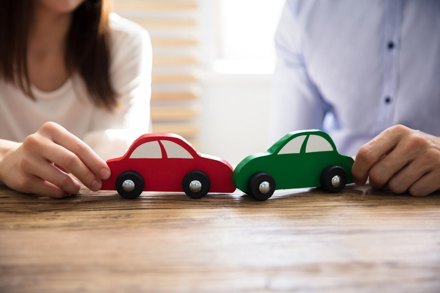 Deux mains poussant une voiture en bois rouge et une voiture en bois verte face a face sur une table